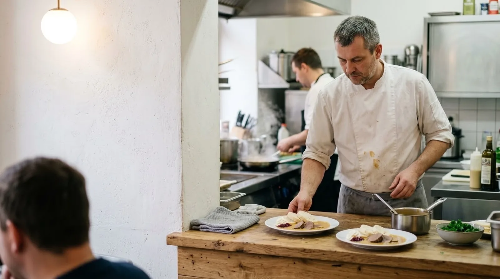 Kuchař v otevřené kuchyni pokládá talíř s poledním menu na výdejní pult